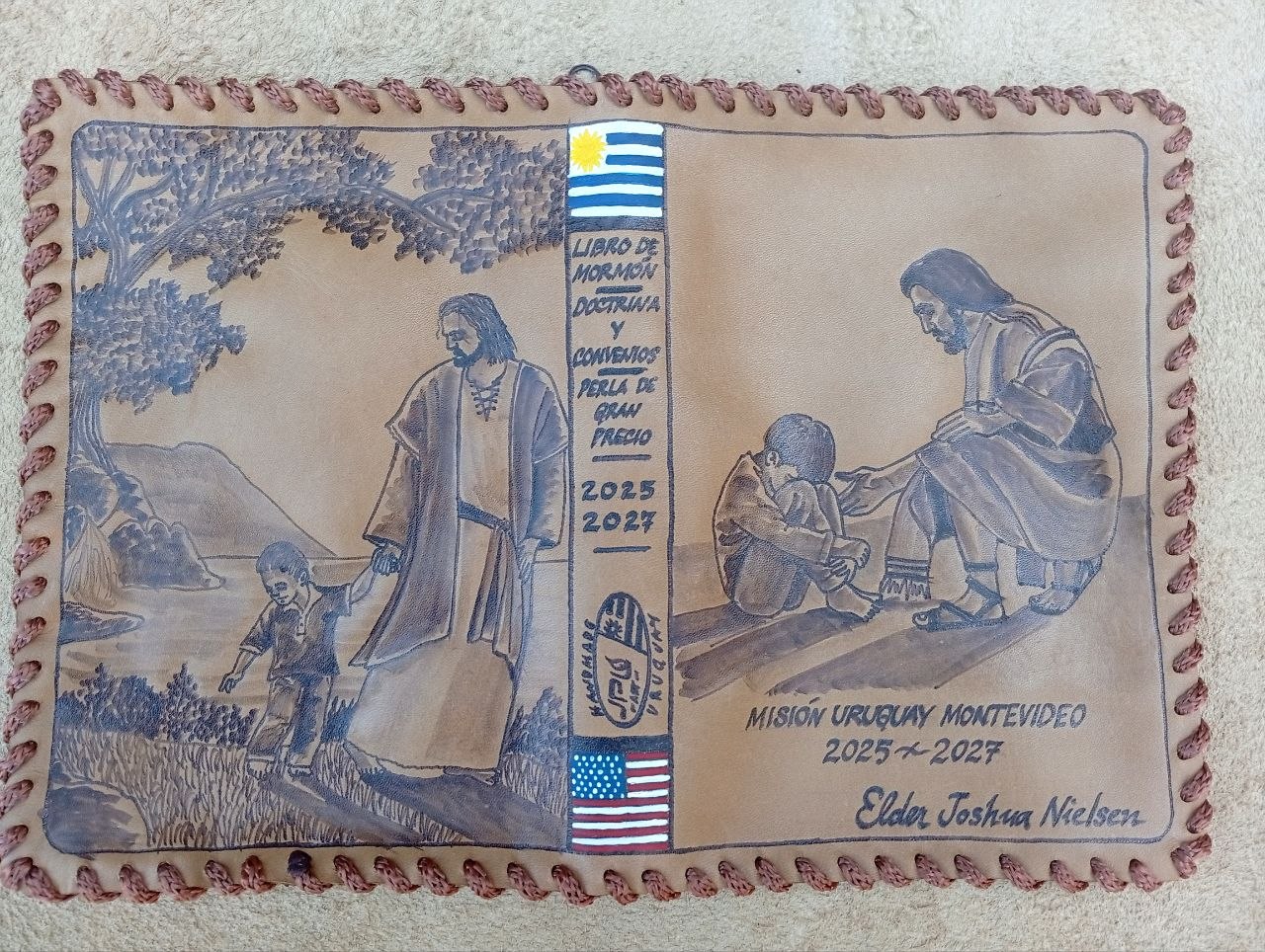 Hand-laced cowhide scripture cover with Christ walking with a child, Christ blessing a child, Uruguay and US flags, and Misión Uruguay Montevideo 2025–2027