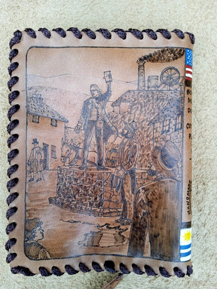 Leather cover with a pyrography of a man speaking from a stone platform in a village