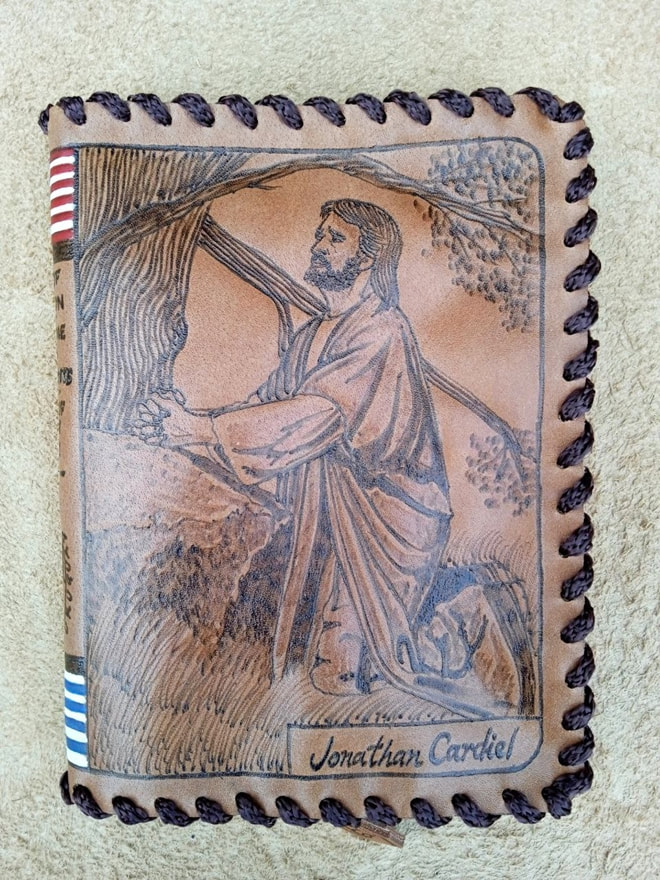 Leather book cover with a pyrography of a man kneeling in prayer under a tree