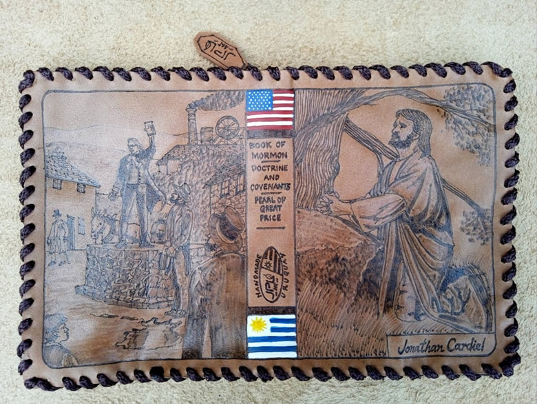 Open leather scripture cover with a village scene, flags of the US and Uruguay, and a kneeling figure under a tree