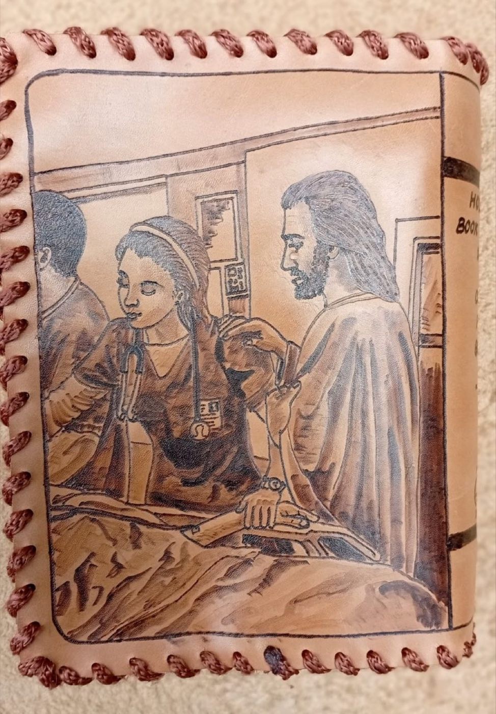 Close view of the Hermana Bluth scripture cover: Christ with a young woman in medical scrubs at a bedside, burned into cowhide